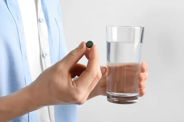 Mujer sosteniendo espirulina píldora y vaso de agua, primer plano —  Fotos de Stock