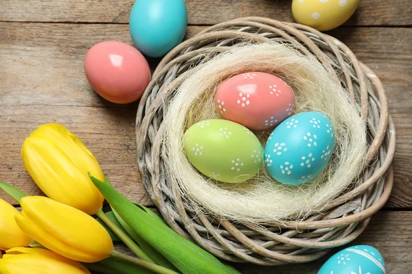 Composition plate de nid d'osier avec œufs de Pâques peints et tulipes sur table en bois — Photo