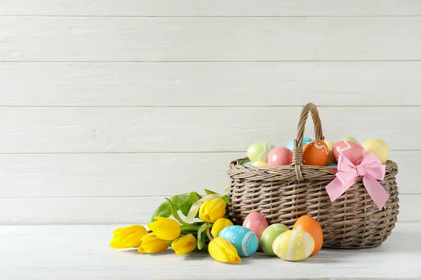 Panier en osier avec œufs de Pâques peints et fleurs de printemps sur la table, espace pour le texte — Photo