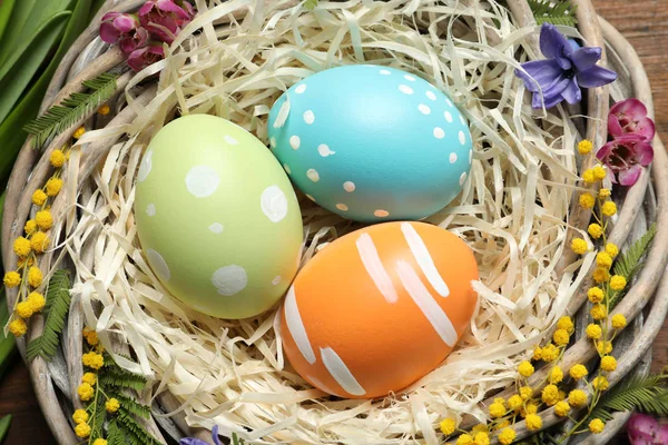 Nid d'osier avec œufs de Pâques peints et fleurs sur la table, gros plan — Photo