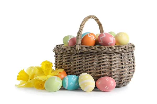 Плетеная корзина с окрашенными пасхальными яйцами и весенними цветами на белом фоне — стоковое фото