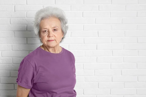 Portrét starší ženy poblíž cihlová zeď. Prostor pro text — Stock fotografie
