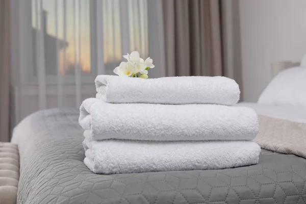 Montón de toallas frescas con flores en la cama en la habitación de hotel — Foto de Stock