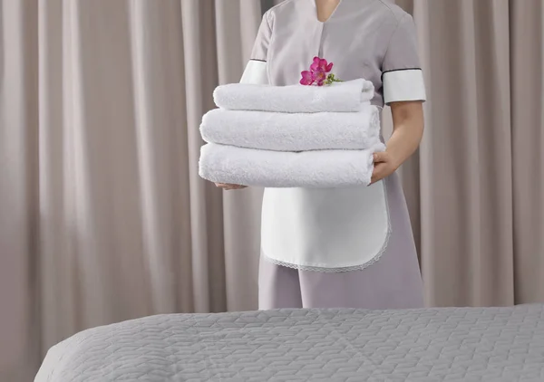 Mucama sosteniendo toallas frescas con flores en la habitación del hotel, primer plano — Foto de Stock