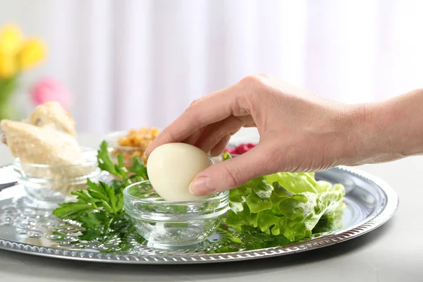 Mujer sosteniendo huevo tradicional sobre la pascua (Pesaj) Seder plato en la mesa, primer plano — Foto de Stock