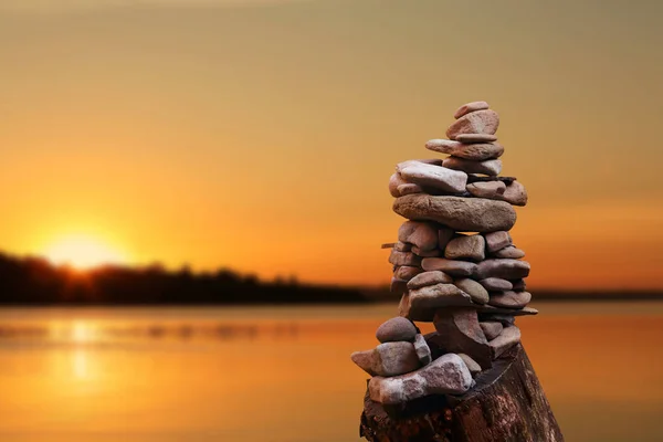 Pilha de pedras tradicionais perto do rio contra belo pôr do sol, espaço para texto. Zen, equilíbrio, harmonia — Fotografia de Stock