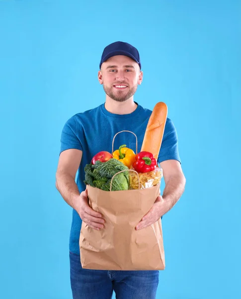 Liefermann hält Papiertüte mit Lebensmitteln auf farbigem Hintergrund — Stockfoto