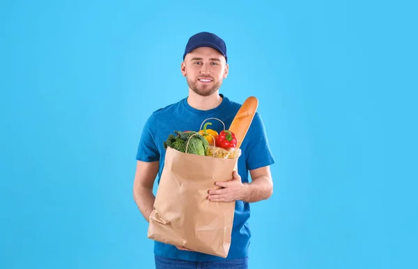 Liefermann hält Papiertüte mit Lebensmitteln auf farbigem Hintergrund — Stockfoto