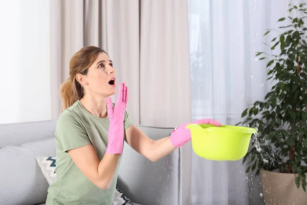 Woman collecting leaking water from ceiling in living room. Time to call plumber