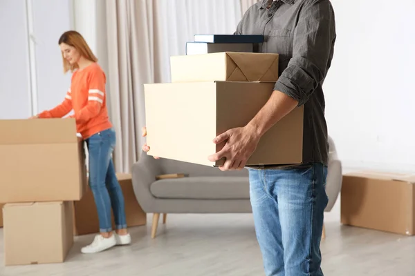 Mann trägt Umzugskartons, während Frau andere in neuem Haus auspackt — Stockfoto