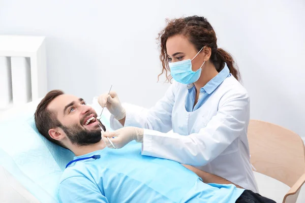 Dentista examinando dentes de jovem com espelho e sonda no hospital — Fotografia de Stock