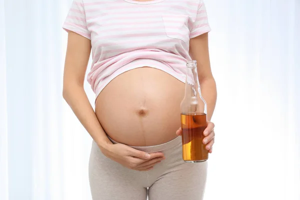 Pregnant woman with bottle of whiskey on light background. Alcohol addiction — Stock Photo, Image