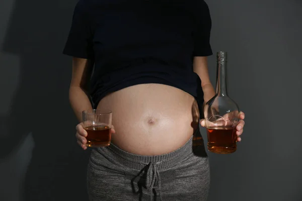 Pregnant woman with glass and bottle of whiskey on dark background. Alcohol addiction — Stock Photo, Image