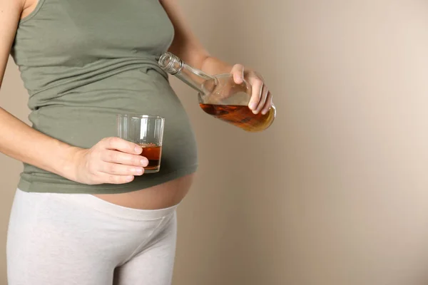 Pregnant woman pouring whiskey into glass on color background. Alcohol addiction — Stock Photo, Image