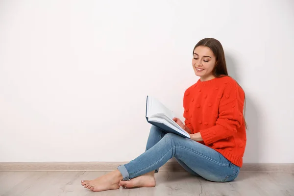 Jeune femme lisant le livre sur le sol près du mur, espace pour le texte — Photo