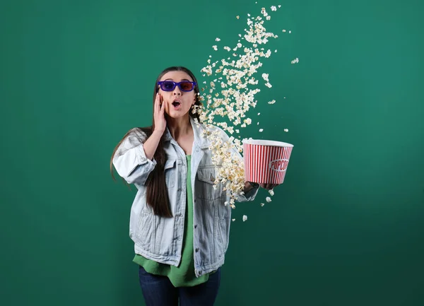 Mujer joven emocional con gafas 3D lanzando palomitas de maíz en el fondo de color —  Fotos de Stock