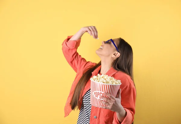 Mujer joven con gafas 3D comiendo palomitas de maíz sabrosas en el fondo de color —  Fotos de Stock