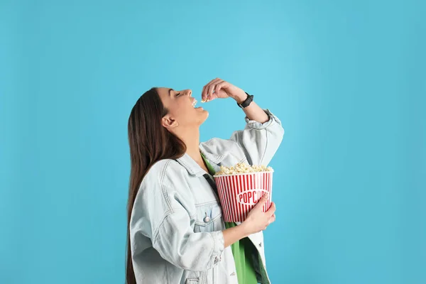 Junge Frau isst leckeres Popcorn auf farbigem Hintergrund — Stockfoto