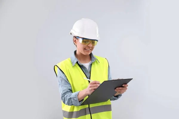Wirtschaftsingenieurin in Uniform mit Klemmbrett auf hellem Hintergrund. Sicherheitsausrüstung — Stockfoto