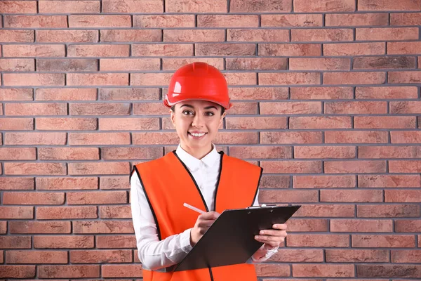 Wirtschaftsingenieurin in Uniform mit Klemmbrett auf Ziegelwand-Hintergrund. Sicherheitsausrüstung — Stockfoto