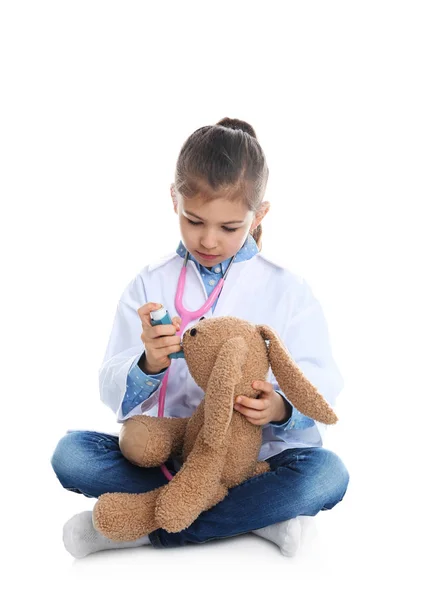 Симпатичный ребенок играет в доктора с мягкой игрушкой на белом фоне — стоковое фото
