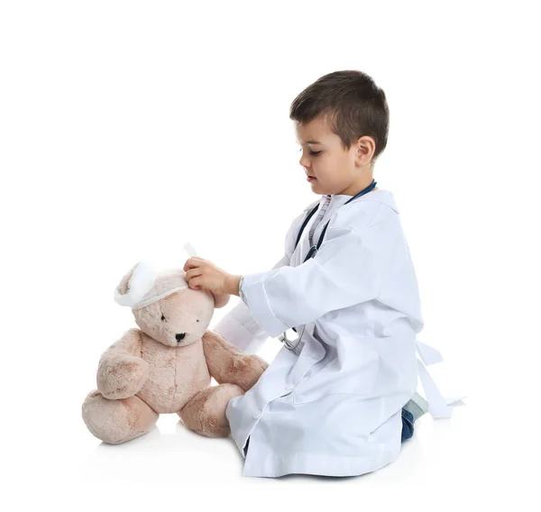 Bonito criança brincando médico com brinquedo de pelúcia no fundo branco — Fotografia de Stock