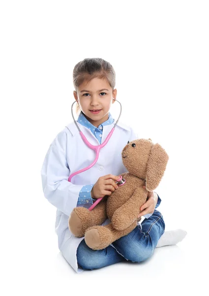 Bonito criança brincando médico com brinquedo de pelúcia no fundo branco — Fotografia de Stock