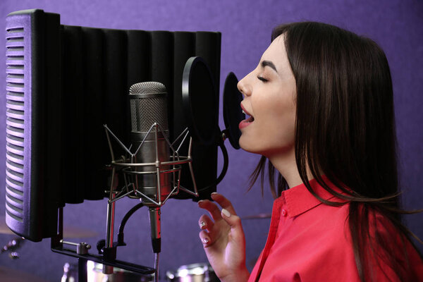 Young singer with microphone recording song in studio