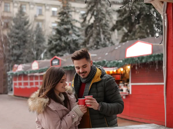 Young couple with cups of mulled wine at winter fair. Space for text — Stock Photo, Image