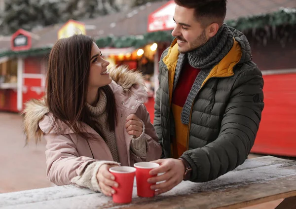 Young couple with cups of mulled wine at winter fair — Stock Photo, Image