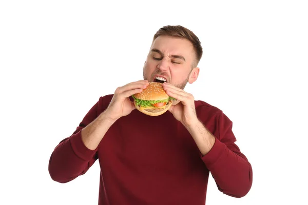 Young man eating tasty burger on white background — Stock Photo, Image