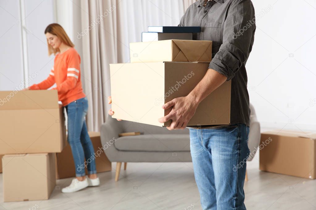 Man carrying moving boxes while woman unpacking other in new house
