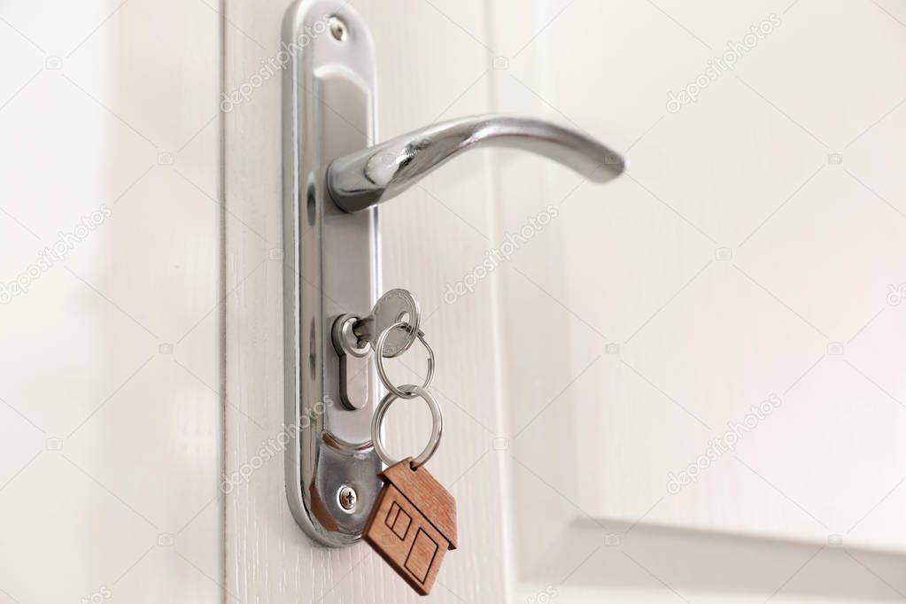 Key with house-shaped trinket in door lock, closeup. Space for text
