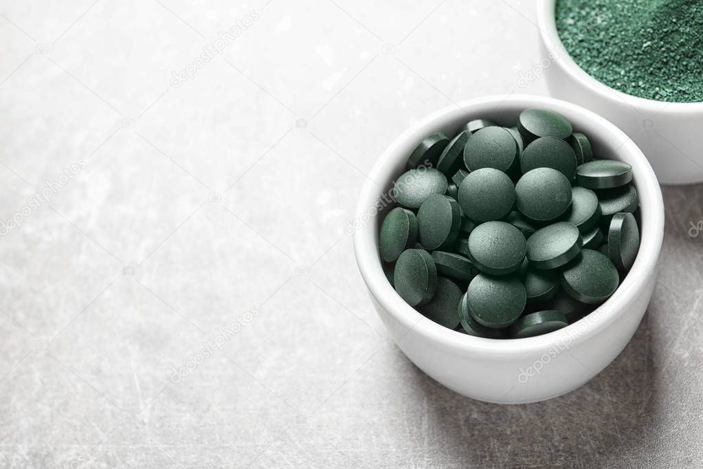 Bowls of spirulina pills and powder on color background, space for text