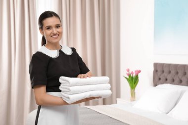Otel odasında temiz havlu yığını tutan genç hizmetçi. Metin için yer