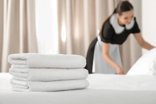 Mladá služka tvorby posteli v hotelovém pokoji, zaměření na zásobník ručníků — Stock fotografie