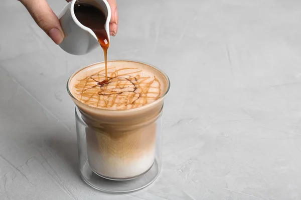 Woman adding caramel syrup to latte macchiato on table, space for text — Stock Photo, Image