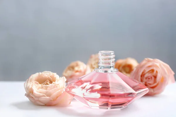 Botella de perfume con hermosas rosas en la mesa — Foto de Stock