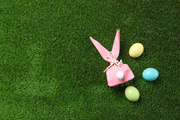 Flache Komposition aus Osterhasen-Geschenktüte und gefärbten Eiern auf grünem Gras, Platz für Text — Stockfoto