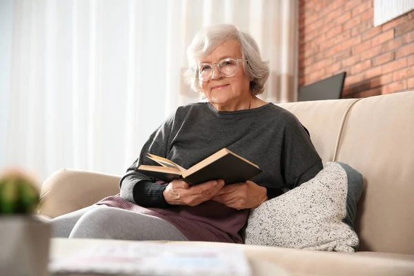 Starsza kobieta, czytając książkę na kanapie w salonie — Zdjęcie stockowe