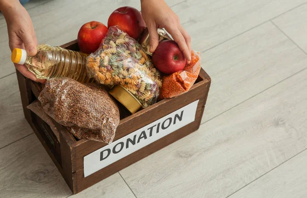 Жінка бере їжу з коробки пожертвувань на дерев'яній підлозі, крупним планом — стокове фото