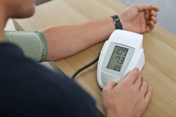 Mann kontrolliert Blutdruck mit Blutdruckmessgerät am Tisch drinnen, Nahaufnahme. Kardiologie-Konzept — Stockfoto