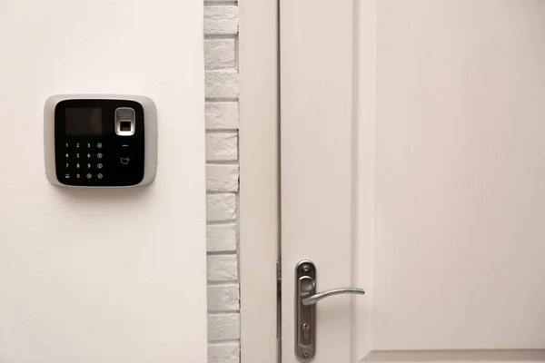 Modern alarm system with fingerprint scanner near entrance indoors. Space for text