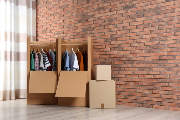 Wardrobe boxes with clothes against brick wall indoors. Space for text