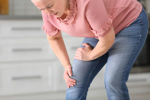 Mulher idosa que sofre de dor no joelho na cozinha. Espaço para texto — Fotografia de Stock
