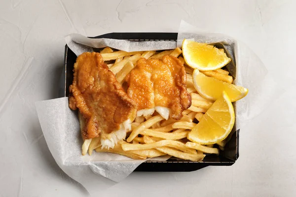 Recipiente com peixe tradicional britânico e batatas fritas no fundo claro, vista superior — Fotografia de Stock