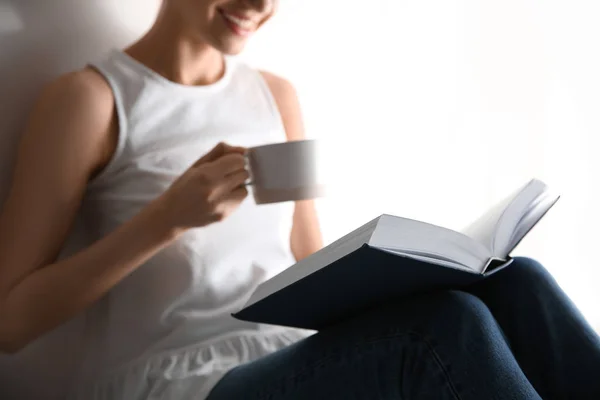 Giovane donna con tazza di caffè lettura libro su sfondo chiaro, primo piano — Foto Stock