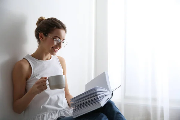 Giovane donna con una tazza di caffè lettura libro a casa, spazio per il testo — Foto Stock
