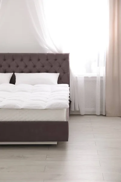 Wygodne łóżko z nowym materacem w pobliżu okna w pokoju. Zdrowy sen — Zdjęcie stockowe