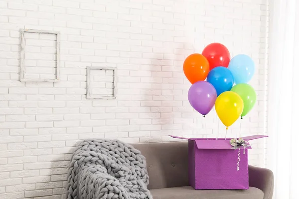 Geschenkbox mit hellen Luftballons auf Sofa vor weißer Ziegelwand. Raum für Text — Stockfoto